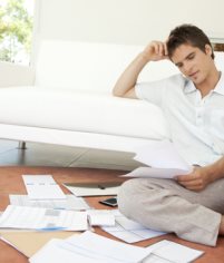 Young man working on his finances, sitting on the floor by the sofa.